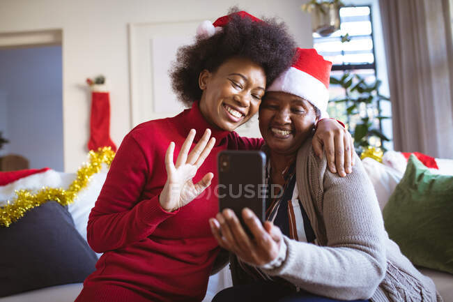 Heureuse femme âgée afro-américaine et fille adulte en chapeaux Santa faire appel vidéo de Noël. Noël, fête et technologie de la communication. — Photo de stock