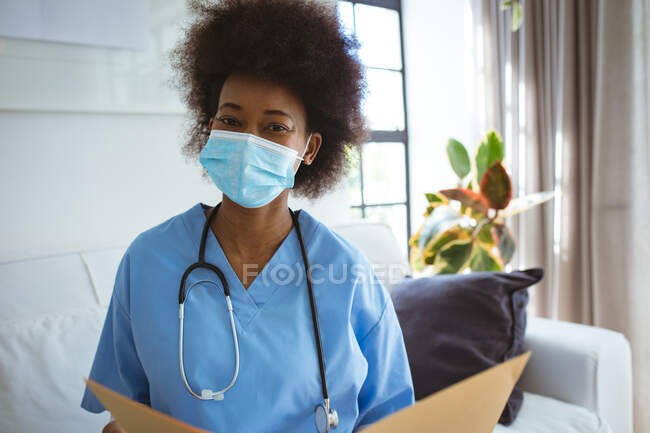 Портрет африканской женщины-врача в маске для лица с документами. здравоохранение и образ жизни во время пандемии ковида 19. — стоковое фото