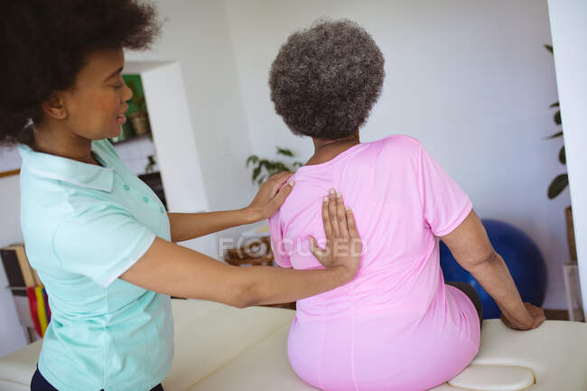 Fisioterapeuta afro-americana a tratar costas de uma paciente idosa na clínica. cuidados de saúde seniores e tratamento de fisioterapia médica. — Fotografia de Stock