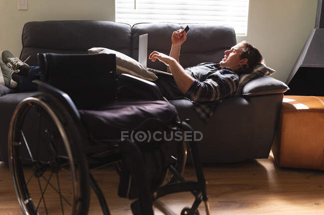 Кавказький інвалід, лежачи вдома на дивані, користується ноутбуком. інвалідність і гандикап — стокове фото