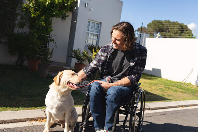 Кавказький інвалід з собакою сидить на інвалідному візку на дорозі. інвалідність і гандикап — стокове фото