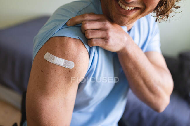Parte centrale di un disabile caucasico che mostra la spalla vaccinata a casa. vaccinazione per la prevenzione del concetto di epidemia di coronavirus — Foto stock