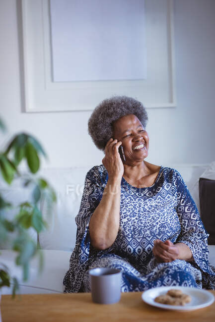 Усміхаючись афроамериканська старша жінка розмовляє по смартфону. витрачати час вдома, використовуючи тільки технології . — стокове фото
