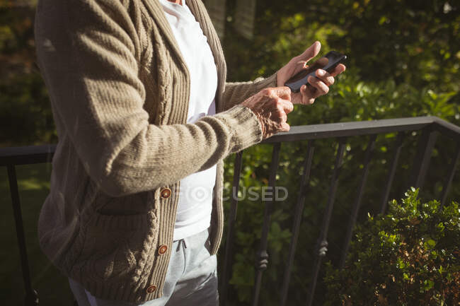 Mann mit Smartphone auf Balkon an sonnigem Tag. Zeit allein zu Hause verbringen. — Stockfoto