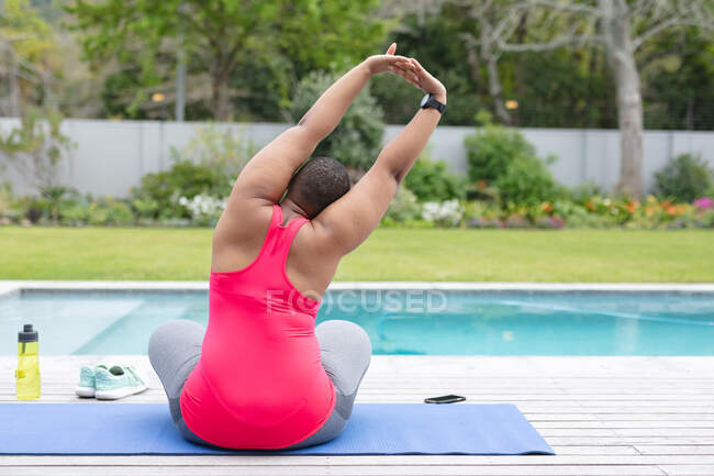 Visão traseira da americana africana plus size mulher em roupas esportivas praticando ioga no jardim. fitness e estilo de vida saudável e ativo. — Fotografia de Stock