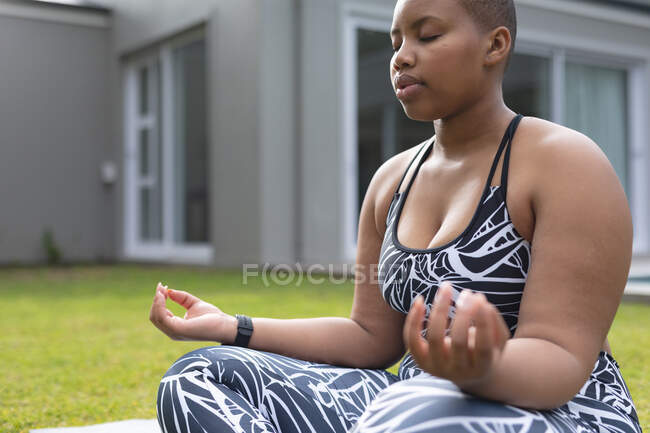 Africano americano enfocado más mujer del tamaño que practica yoga en estera en jardín. fitness y estilo de vida saludable y activo. - foto de stock