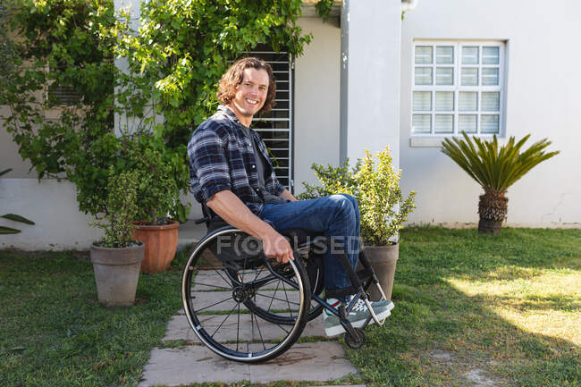 Retrato de hombre caucásico discapacitado sentado en silla de ruedas sonriendo en el jardín. concepto de discapacidad y discapacidad - foto de stock