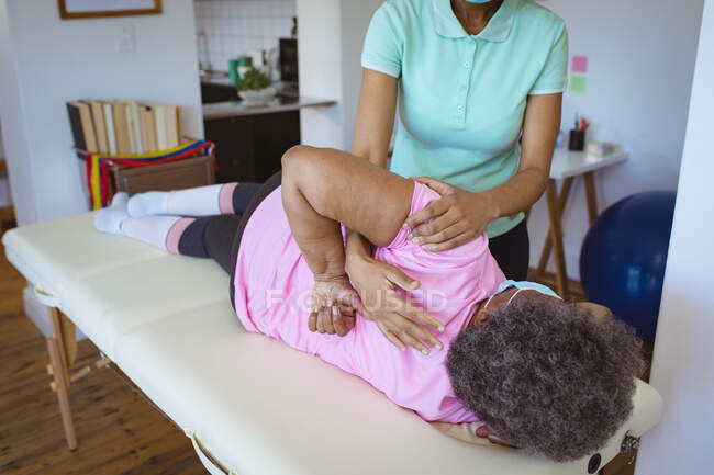 Eine afroamerikanische Physiotherapeutin behandelt eine ältere Patientin mit Gesichtsmasken in einer Klinik. Senior Health und medizinische physiotherapeutische Behandlung. — Stockfoto