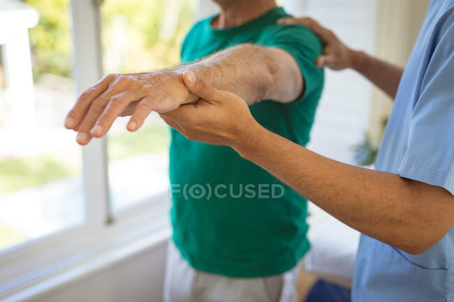 Fisioterapeuta Biracial masculino que trata los brazos de un paciente masculino mayor en la clínica. atención médica de alto nivel y tratamiento de fisioterapia médica. - foto de stock