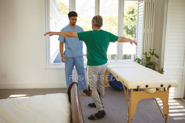 Fisioterapista maschile Biraciale che guarda il paziente di sesso maschile anziano in clinica. assistenza sanitaria senior e trattamento fisioterapico medico. — Foto stock