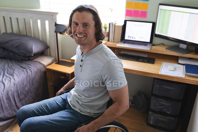 Портрет кавказского инвалида, сидящего на инвалидной коляске и улыбающегося дома. Концепция инвалидности и инвалидности — стоковое фото