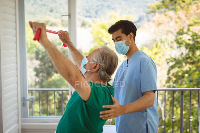 Biracial male physiotherapist with face mask treating back of senior male patient at clinic. senior healthcare and medical physiotherapy treatment. — Stock Photo