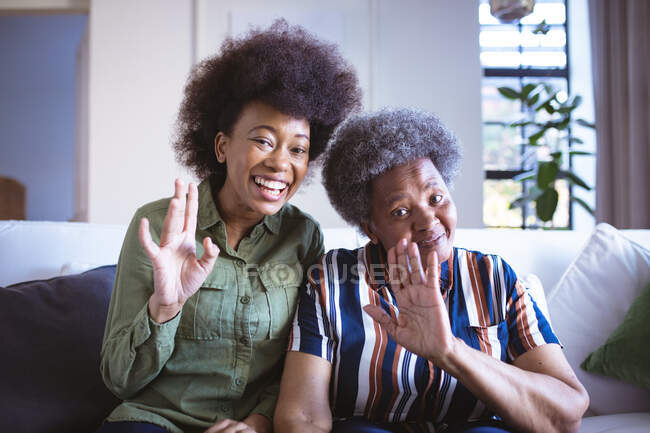 Portrait d'une femme âgée afro-américaine souriante avec sa fille adulte agitant le bras. temps en famille à la maison ensemble. — Photo de stock