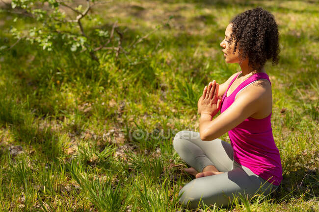Relaxing biracial woman practicing yoga, sitting with crossed legs and meditating in countryside. healthy, active outdoor lifestyle and leisure time. — Stock Photo