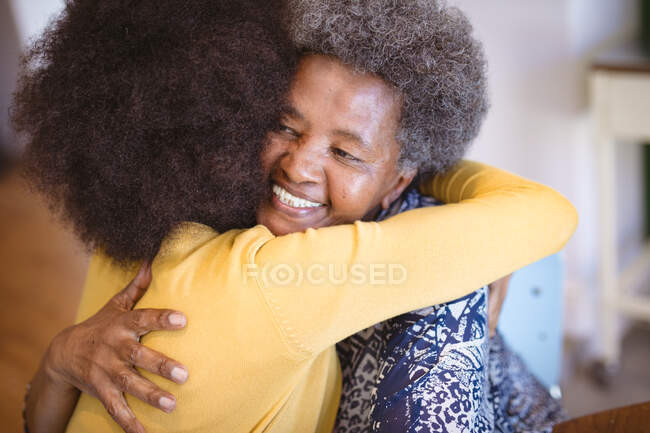 Smiling african american senior woman with adult daughter sitting and embracing. family time at home together. — Stock Photo