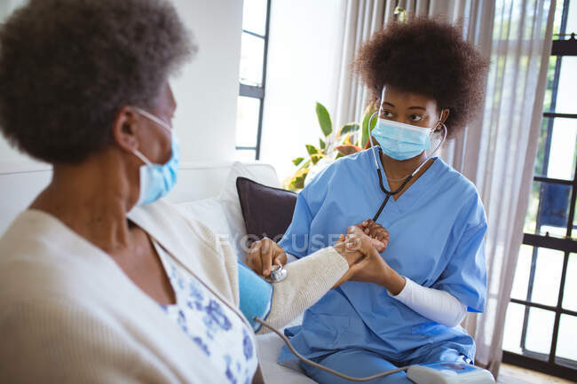 Médica afro-americana com máscara facial tratando a paciente idosa em casa. cuidados de saúde e estilo de vida durante a pandemia de 19 pessoas. — Fotografia de Stock