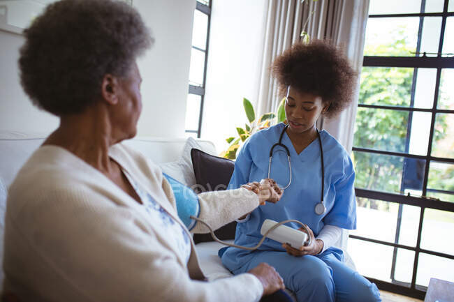 African american female doctor treating senior female patient at home. healthcare and lifestyle during covid 19 pandemic. — Stock Photo