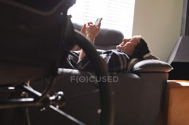 Кавказький інвалід, лежачи на дивані, користується смартфоном. інвалідність і гандикап — стокове фото