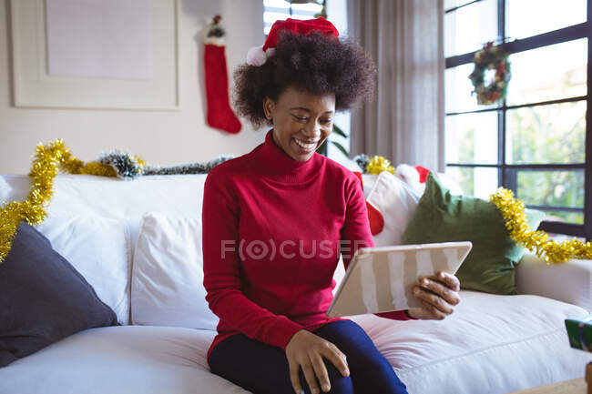 Mujer afroamericana feliz en santa hat haciendo videollamada de Navidad tableta. navidad, festividad y tecnología de la comunicación. - foto de stock