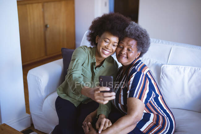 Усміхнена афроамериканська старша жінка з дорослою дочкою бере селфі зі смартфоном. сімейний час вдома, використовуючи технології разом . — стокове фото