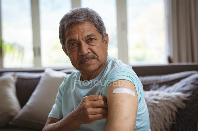 Portrait d'un homme âgé biracial montrant un bandage sur le bras après une vaccination covid. soins de santé et mode de vie pendant la pandémie de covide 19. — Photo de stock