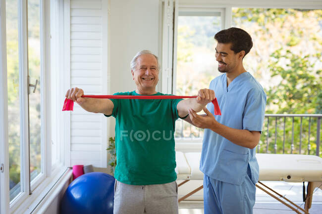 Smiling biracial fisioterapeuta masculino tratar costas de paciente do sexo masculino sênior na clínica. cuidados de saúde seniores e tratamento de fisioterapia médica. — Fotografia de Stock
