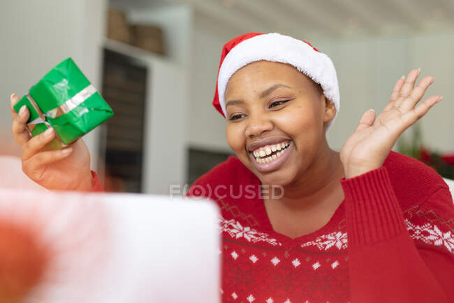 Feliz afroamericana más mujer de tamaño en sombrero de santa haciendo videollamada de Navidad en el ordenador portátil. navidad, festividad y tecnología de la comunicación. - foto de stock