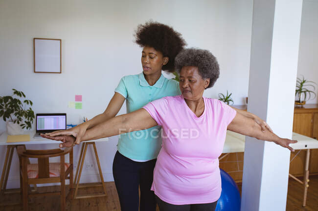 Fisioterapeuta afroamericana que trata los brazos de una paciente mayor en la clínica. atención médica de alto nivel y tratamiento de fisioterapia médica. - foto de stock
