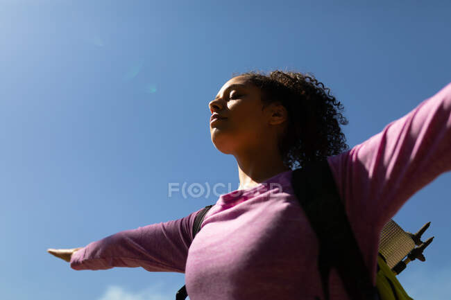 Mujer Biracial con mochila de pie con los brazos abiertos. estilo de vida al aire libre saludable y activo y tiempo libre. - foto de stock
