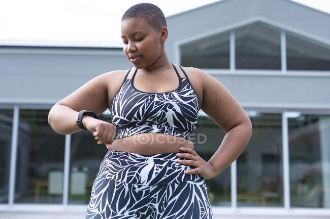 Afroamericano plus size donna indossa abiti sportivi e controllo smartwatch. fitness e stile di vita sano e attivo. — Foto stock
