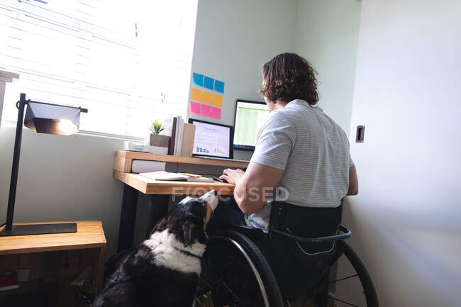 Kaukasischer behinderter Mann, der im Rollstuhl sitzt und von zu Hause aus mit Laptop arbeitet. Behinderten- und Behindertenkonzept — Stockfoto