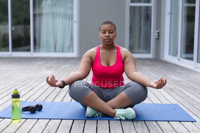Afroamerikanische Plus-Size-Frau in Sportkleidung sitzt auf Matte und praktiziert Yoga. Fitness und gesunder, aktiver Lebensstil. — Stockfoto