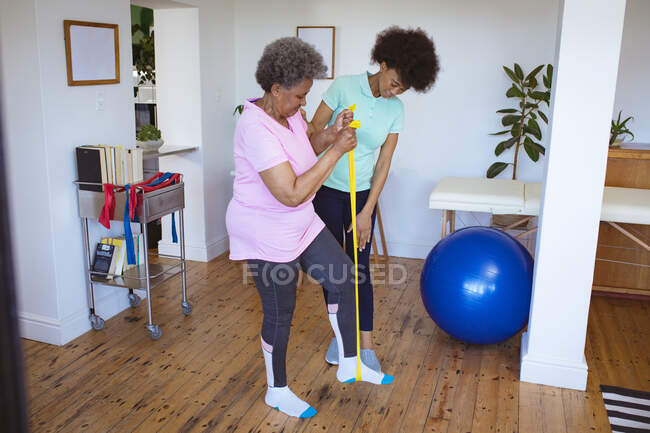 Afro-americana fisioterapeuta do sexo feminino tratando perna de paciente sênior na clínica. cuidados de saúde seniores e tratamento de fisioterapia médica. — Fotografia de Stock
