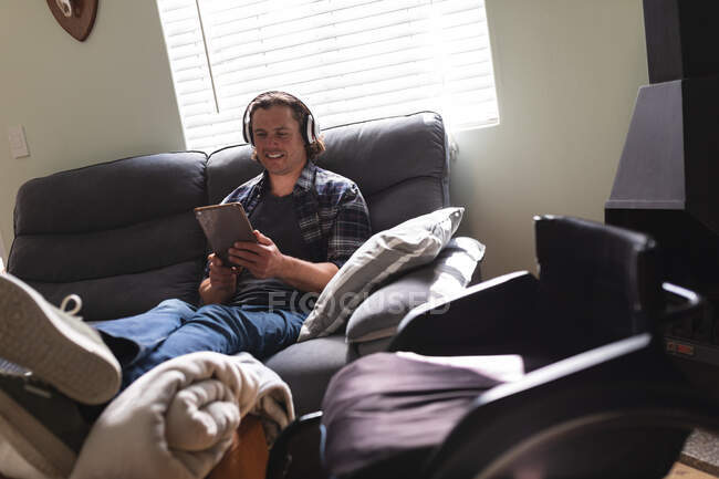 Caucasian disabled man wearing headphones using digital tablet sitting on the couch at home. disability and handicap concept — Stock Photo