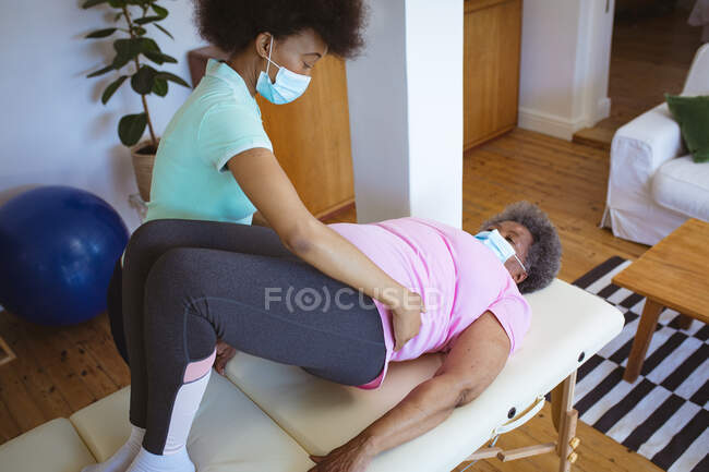 African american female physiotherapist treating senior female patient with face masks at clinic. senior healthcare and medical physiotherapy treatment. — Stock Photo