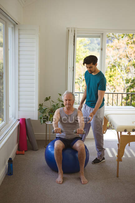 Birassische männliche Physiotherapeutin, die einen älteren männlichen Patienten in der Klinik behandelt. Senior Health und medizinische physiotherapeutische Behandlung. — Stockfoto