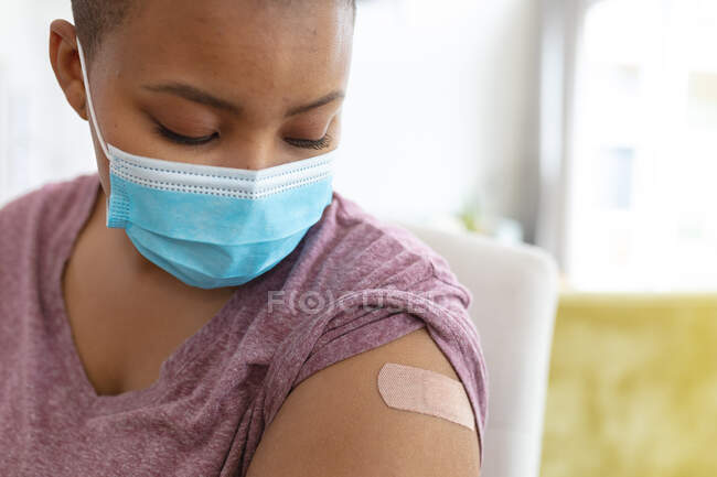 African american plus size woman in face mask showing arm with plaster after vaccination. health and lifestyle during covid 19 pandemic. — Stock Photo