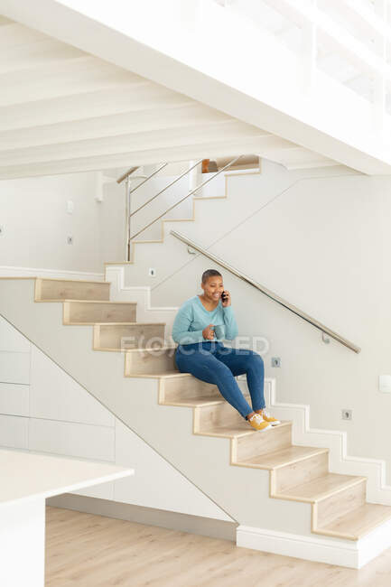 Счастливый африканский американец плюс размер женщина делает звонок и пить кофе на лестнице. образ жизни, отдых, проведение времени дома с технологиями. — стоковое фото