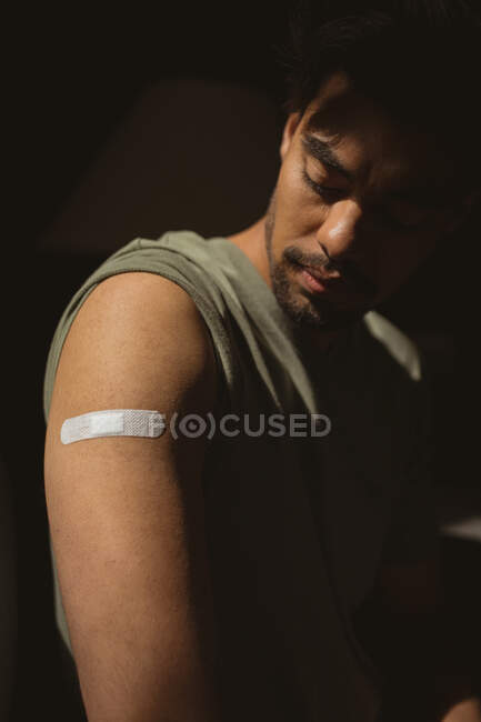 Primer plano del hombre biracial que muestra vendaje en el brazo después de la vacunación covid. salud y estilo de vida durante la pandemia de covid 19. - foto de stock
