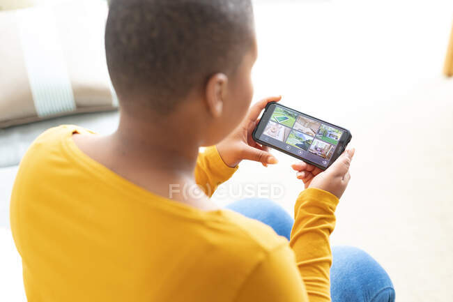 Back view of african american plus size woman checking view from security cameras on smartphone. safety, security and technology at home. — Stock Photo