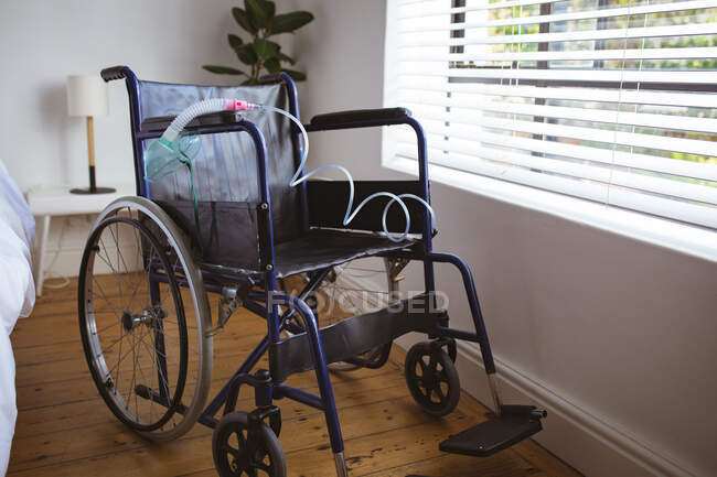 Empty wheelchair with hanging oxygen mask in bedroom at home. healthcare and lifestyle during covid 19 pandemic. — Stock Photo