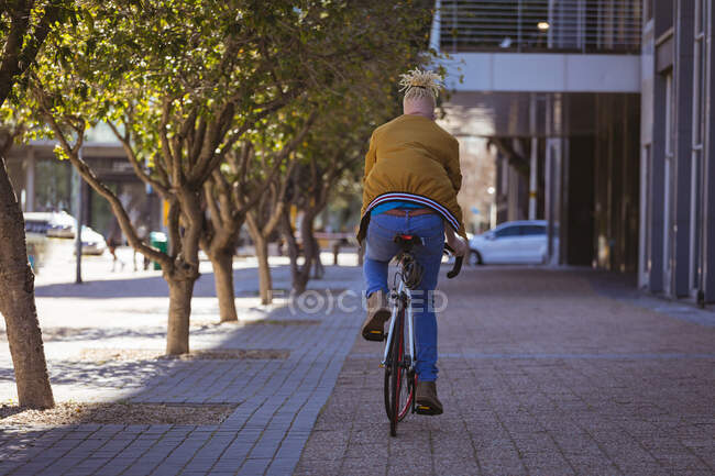 Hombre afroamericano albino con rastas montando en bicicleta. sobre la marcha, fuera y alrededor de la ciudad. - foto de stock