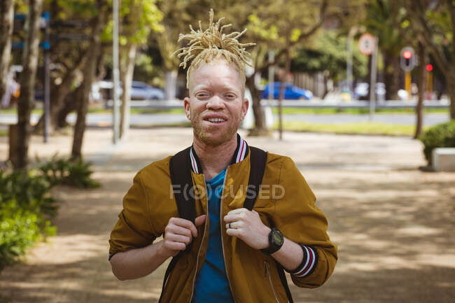 Ritratto di sorridente uomo afroamericano albino con dreadlocks che guarda la macchina fotografica. in movimento, in giro per la città. — Foto stock