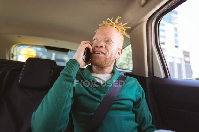 Heureux albinos homme afro-américain avec dreadlocks assis dans la voiture parler sur smartphone. nomade numérique en déplacement, en déplacement dans la ville. — Photo de stock