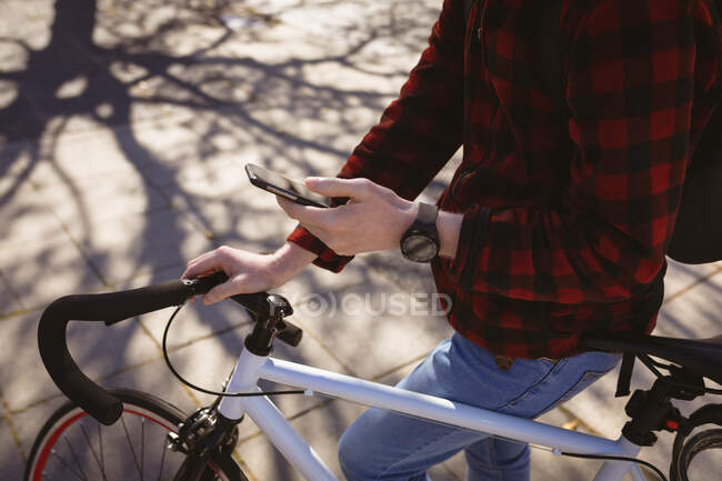 Hombre en bicicleta usando teléfono inteligente. nómada digital sobre la marcha, fuera y alrededor de la ciudad. - foto de stock