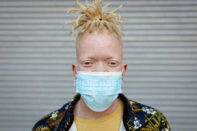 Retrato do homem americano africano albino com dreadlocks usando máscara facial. em movimento, para fora e sobre na cidade durante a pandemia covid 19. — Fotografia de Stock