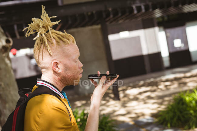 Happy albino african american man with dreadlocks on street talking on smartphone. digital nomad on the go, out and about in the city. — Stock Photo