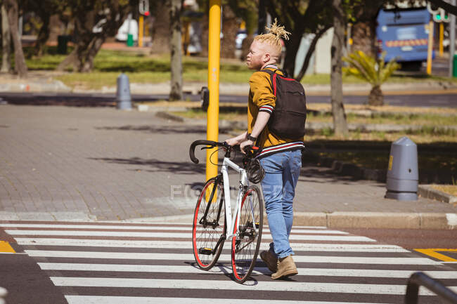 Задумчивый альбинос африканский американец с дредами, переходящими дорогу на велосипеде. on the go, out and about in the city. — стоковое фото