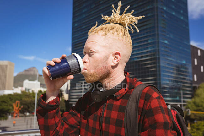 Hombre afroamericano albino con rastas bebiendo café para llevar. sobre la marcha, fuera y alrededor de la ciudad. - foto de stock