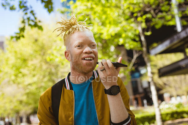 Щасливий альбіноамериканський чоловік з дредлоками в парку розмовляє по смартфонах. цифровий кочівник на ходу, вихід і близько в місті . — стокове фото